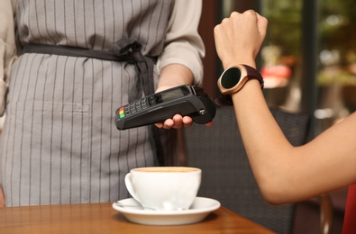 Photo of Woman making payment with smart watch in cafe, closeup
