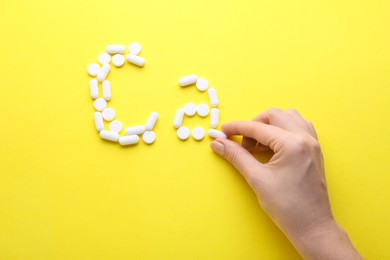 Woman making calcium symbol with white pills on yellow background, top view