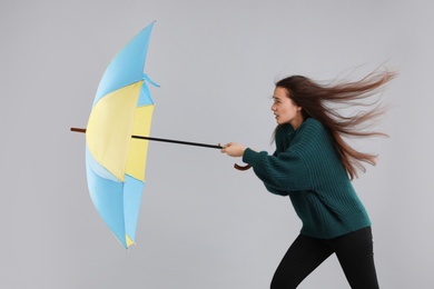 Woman with umbrella caught in gust of wind on grey background