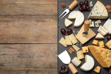 Cheese platter with specialized knives and fork on wooden table, top view. Space for text