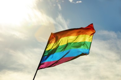 Bright LGBT flag against blue sky with clouds
