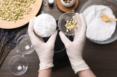 Woman in gloves making bath bomb at wooden table, top view