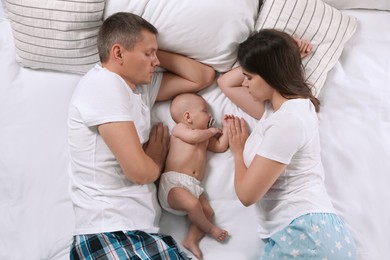 Couple and baby sleeping on bed together, top view