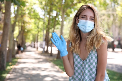Woman in protective face mask showing hello gesture outdoors. Keeping social distance during coronavirus pandemic