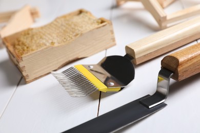 Honeycomb frame and beekeeping tools on white wooden table, closeup