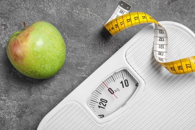 Scales, measuring tape and apple on gray background, closeup. Weight loss