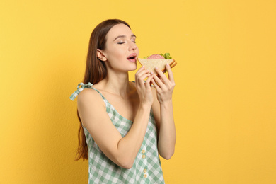 Photo of Young woman eating tasty sandwich on yellow background