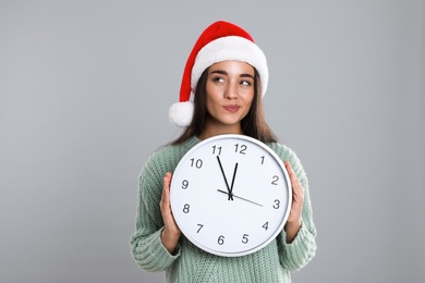 Woman in Santa hat with clock on grey background. New Year countdown