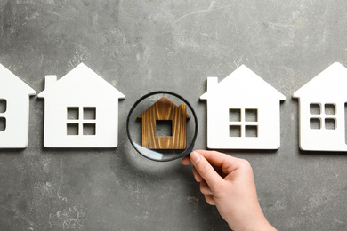 Woman with magnifying glass exploring different house models on grey stone background, top view. Search concept