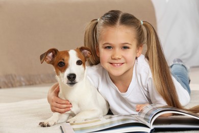 Photo of Cute girl reading book on floor with her dog indoors. Adorable pet