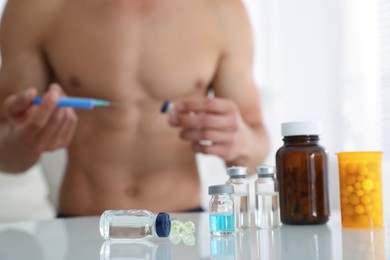 Man filling syringe at table indoors, focus on drugs. Doping concept