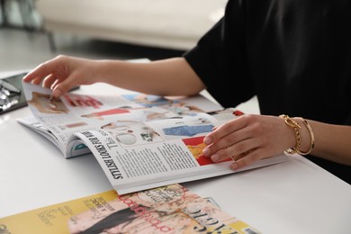 Woman reading fashion magazine at white table indoors, closeup
