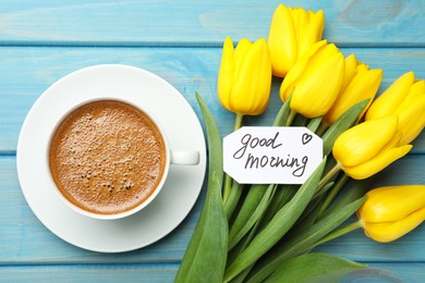 Cup of aromatic coffee, beautiful yellow tulips and Good Morning note on light blue wooden table, flat lay