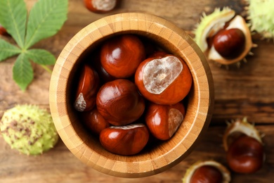 Horse chestnuts in bowl on wooden table, top view