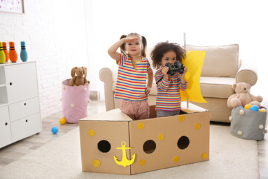 Cute little children playing with cardboard ship and binoculars at home