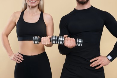 Photo of Athletic people exercising with dumbbells on light brown background, closeup