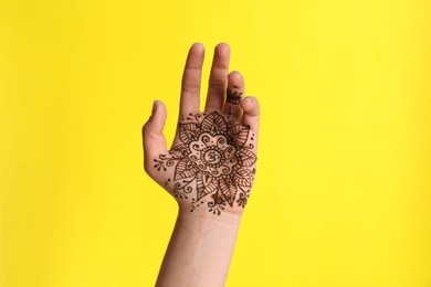Woman with henna tattoo on palm against yellow background, closeup. Traditional mehndi ornament