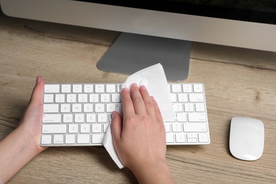 Woman wiping keyboard with paper towel at wooden table, closeup