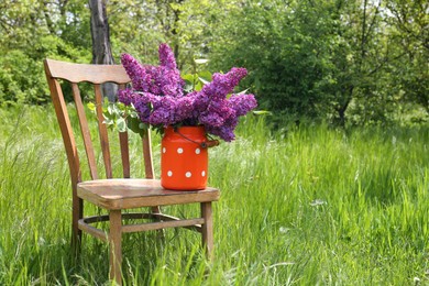 Beautiful lilac flowers in milk can outdoors. Space for text