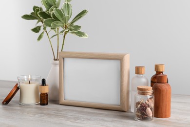 Blank photo frame, different bottles and decor elements on wooden table