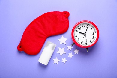 Photo of Red sleep mask, confetti in shape of stars, bottle of cosmetic product and alarm clock on purple background, flat lay