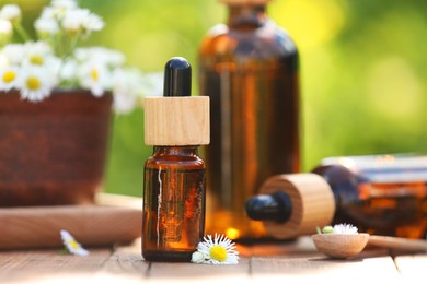 Bottles of chamomile essential oil and flowers on wooden table, closeup