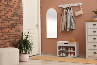 Rack with different shoes near pale pink wall in hall