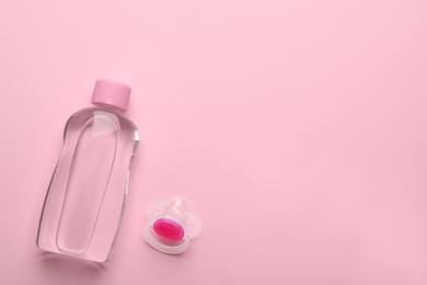 Bottle of baby oil and pacifier on pink background, flat lay. Space for text