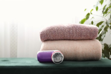 Photo of Modern fabric shaver and woolen sweaters on green bench indoors, space for text