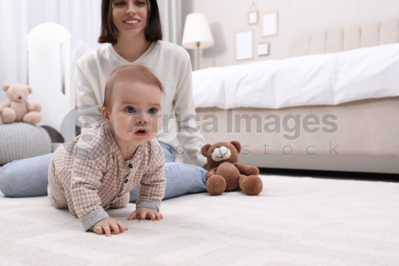 Young mother watching her cute baby crawl on floor at home