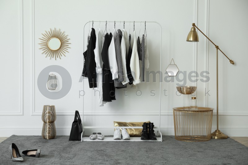 Rack with stylish clothes near white wall in dressing room