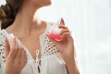 Young woman using perfume indoors, closeup. Space for text