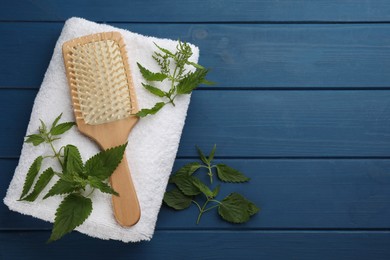 Photo of Stinging nettle, brush and towel on blue wooden background, flat lay with space for text. Natural hair care