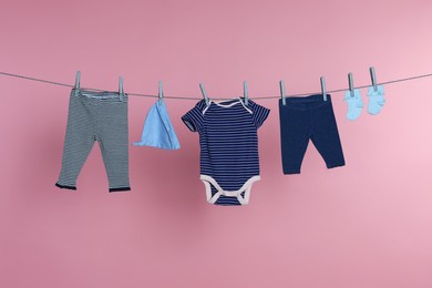 Different baby clothes drying on laundry line against pink background