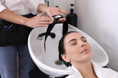 Photo of Professional hairdresser applying conditioner on woman's hair in beauty salon, closeup