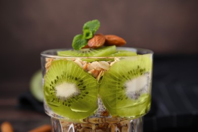 Photo of Delicious dessert with kiwi, muesli and almonds in glass, closeup