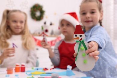 Cute little children with beautiful Christmas crafts at table in room, focus on paper snowman. Space for text