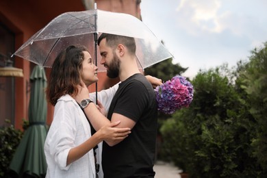 Young couple with umbrella enjoying time together under rain on city street, space for text