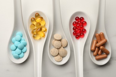 Spoons with different dietary supplements on white table, flat lay