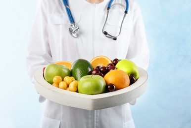 Female doctor holding plate with fresh fruits on light background. Cardiac diet