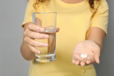 African-American woman with glass of water and vitamin pill on light grey background, closeup