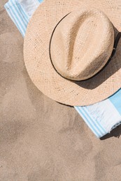 Straw hat and beach towel on sand, top view. Space for text