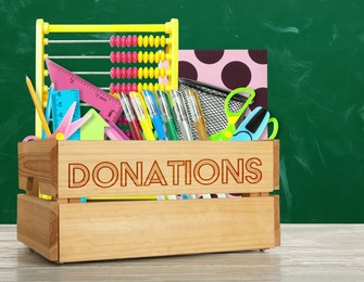 Donation box with different school stationery on white wooden table near chalkboard