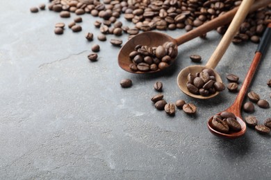 Wooden spoons with roasted coffee beans on grey table, closeup. Space for text