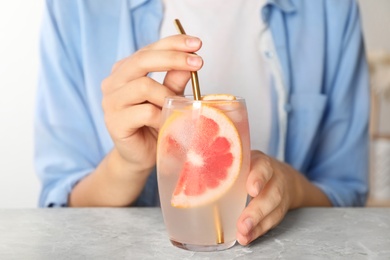 Woman with glass of grapefruit refreshing drink at grey marble table, closeup