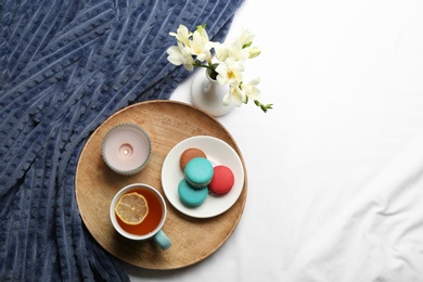Flat lay composition with tea and warm plaid on white bedsheet, space for text