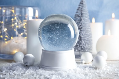 Magical empty snow globe with Christmas decorations and candles on table