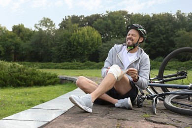 Man applying bandage onto his knee near bicycle outdoors, space for text