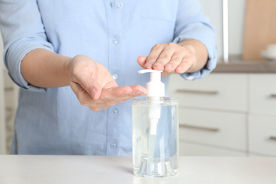 Photo of Woman applying antiseptic gel on hand indoors, closeup