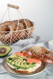 Delicious bagel with cream cheese, salmon, avocado and microgreens on white marble table